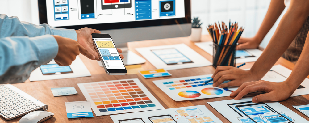 Hands reviewing website layouts and a phone mockup at a worktable
